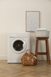 Photo of Laundry room interior with modern washing machine and wooden stool near white wall