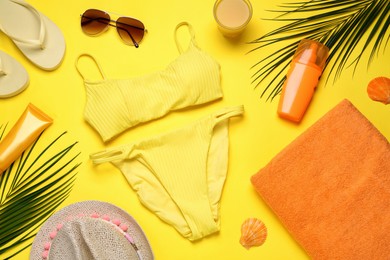 Beach towel, swimsuit, flip flops, hat. sunglasses and sun protection products on yellow background, flat lay