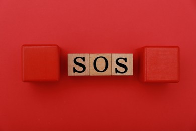Abbreviation SOS made of wooden cubes on red background, flat lay