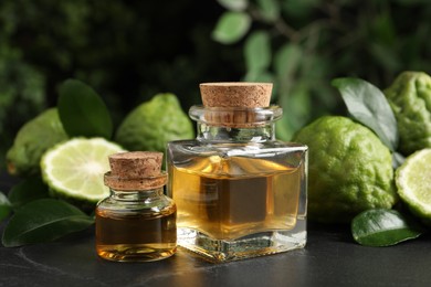 Glass bottles of bergamot essential oil and fresh fruits on black stone table