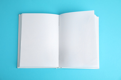 Open book with blank pages on blue background, top view