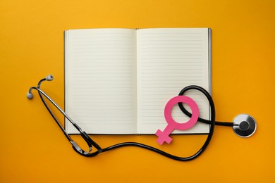 Female gender sign, open notebook and stethoscope on orange background, flat lay. Women's health concept