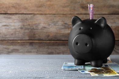 Black piggy bank with money on wooden table, space for text