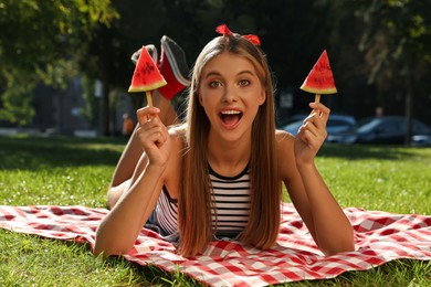 Beautiful girl with pieces of watermelon on picnic blanket in park