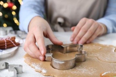 Photo of Woman making Christmas gingerbread man cookies at white table, closeup