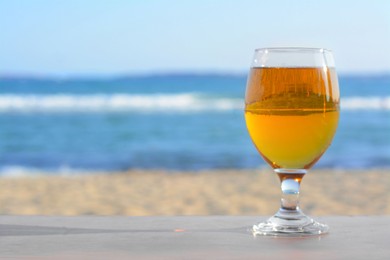 Glass of cold beer on wooden table at beach. Space for text
