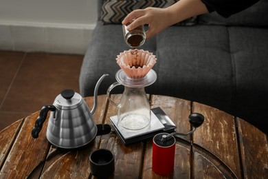 Photo of Barista putting coffee into jug with wave dripper at wooden table in cafe, closeup