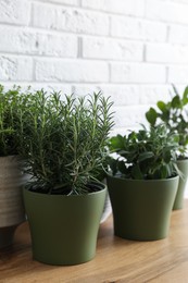 Photo of Different aromatic potted herbs on wooden table near white brick wall