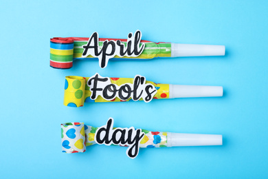 Party horns with words APRIL FOOL'S DAY on light blue background, flat lay