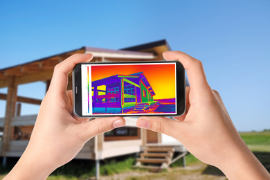 Woman detecting heat loss in house using thermal viewer on smartphone, outdoors. Energy efficiency