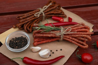 Photo of Bundles of delicious kabanosy with rosemary, peppercorn, garlic and chilli on wooden table