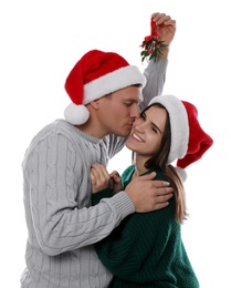Happy man kissing his girlfriend under mistletoe bunch on white background