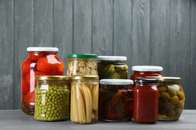 Glass jars with different pickled vegetables on grey wooden background