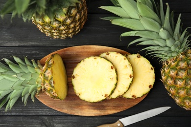 Photo of Whole and cut pineapples on black wooden table, flat lay