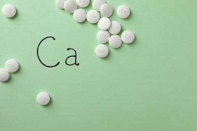 Flat lay composition with calcium supplement pills on light green background, space for text