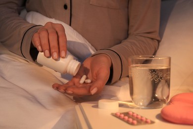 Woman pouring pills from bottle into hand indoors, closeup. Insomnia treatment