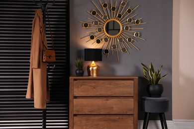 Photo of Wooden chest of drawers with decor, coat stand and mirror in hallway. Interior design