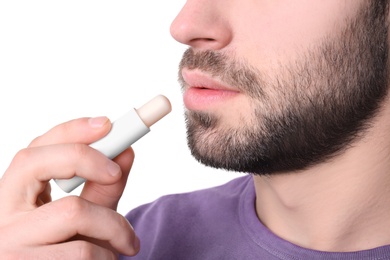 Young man applying cold sore balm on lips against white background, closeup