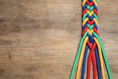 Top view of braided colorful ropes on wooden background, space for text. Unity concept