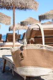 Straw bag with sunglasses on wooden sunbed near sea. Beach accessories