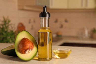 Photo of Fresh avocado and cooking oil on beige marble table in kitchen, space for text