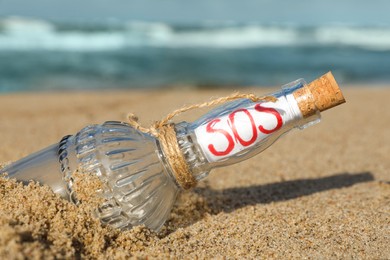 Glass bottle with SOS message on sand near sea, closeup