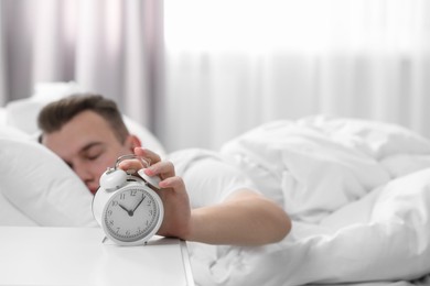 Photo of Sleepy man turning off alarm clock at home in morning, focus on hand. Space for text