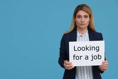 Photo of Unemployed woman holding sign with phrase Looking For A Job on light blue background. Space for text