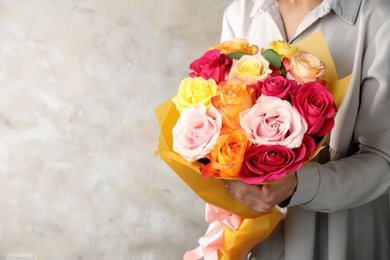 Woman holding luxury bouquet of fresh roses on beige background, closeup. Space for text