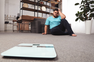 Scales and depressed overweight man on floor at home