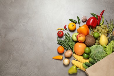 Photo of Paper bag with assortment of fresh organic fruits and vegetables on grey table, flat lay. Space for text