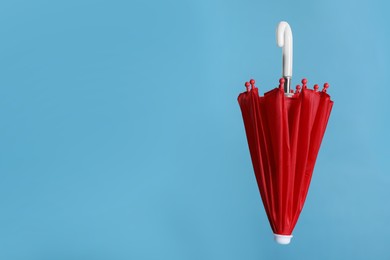 Closed small red umbrella on light blue background. Space for text