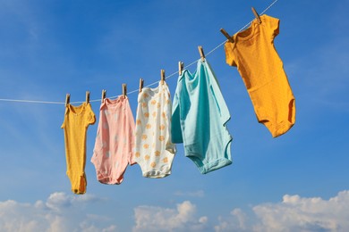 Clean baby onesies hanging on washing line against sky. Drying clothes
