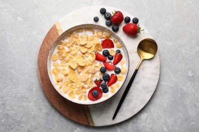 Bowl of tasty crispy corn flakes with milk and berries on light grey table, top view