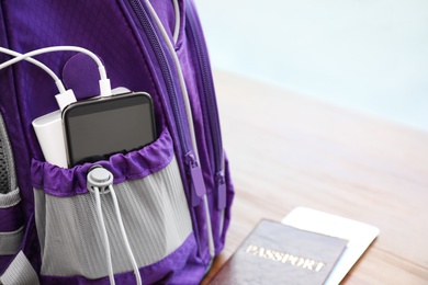 Photo of Charging mobile phone with power bank in purple backpack and passport on table, closeup. Space for text