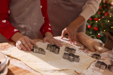 Mother and her daughter making delicious Christmas cookies at wooden table indoors, closeup