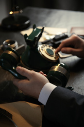 Detective dialing number on vintage telephone at table, closeup