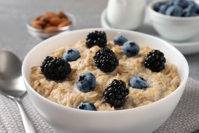 Tasty oatmeal porridge with blackberries and blueberries in bowl on table, closeup