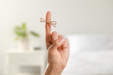 Woman showing index finger with tied bow as reminder indoors, closeup