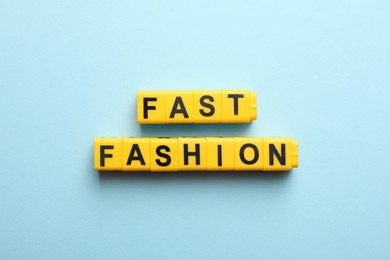 Yellow plastic cubes with phrase Fast Fashion on light blue background, flat lay