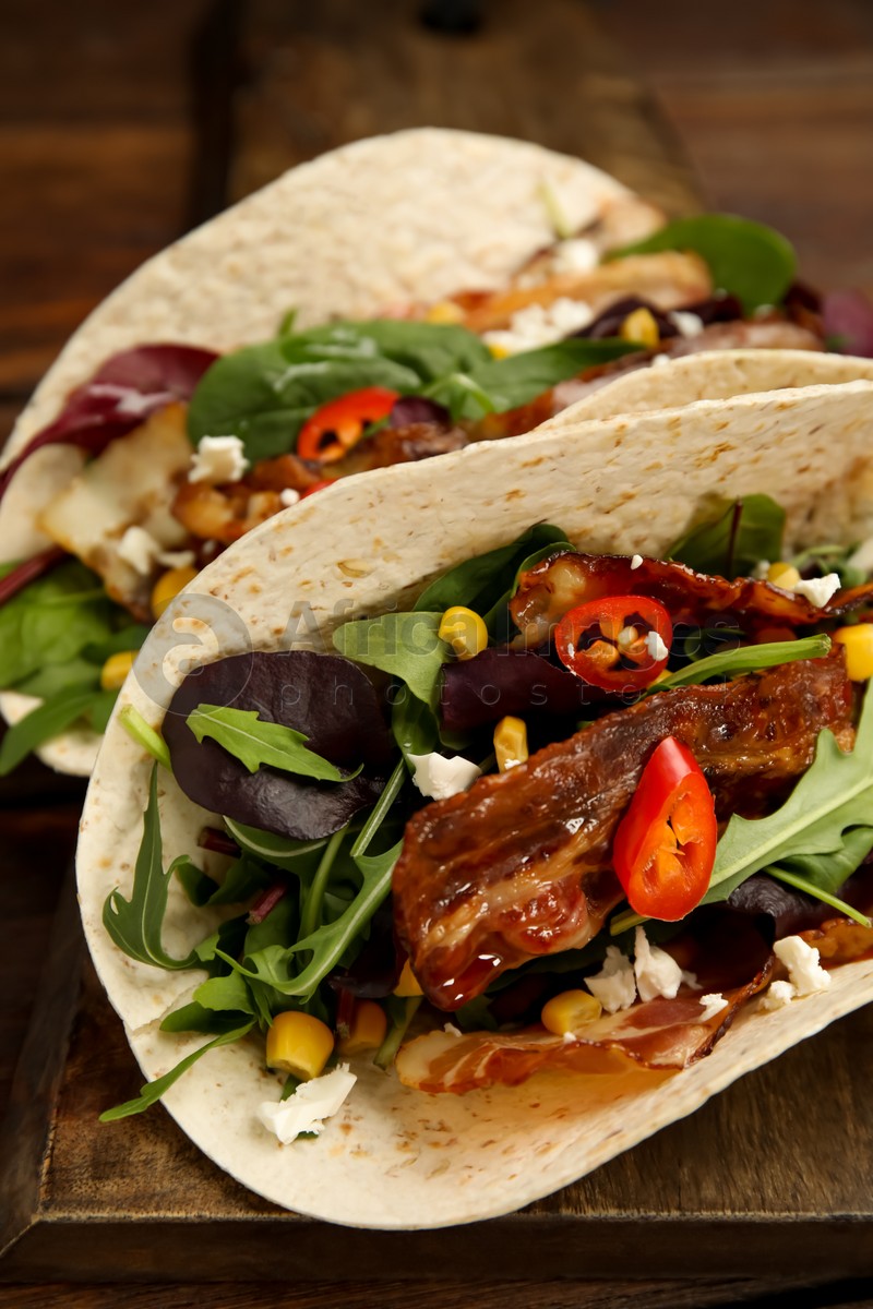 Delicious tacos with fried bacon, vegetables and cheese on wooden board, closeup