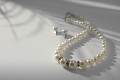 Elegant pearl necklace and earrings on white table, closeup. Space for text