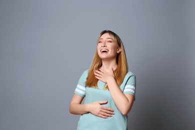 Beautiful young woman laughing on grey background. Funny joke
