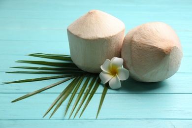 Young peeled coconuts with palm leaf and flower on light blue wooden table