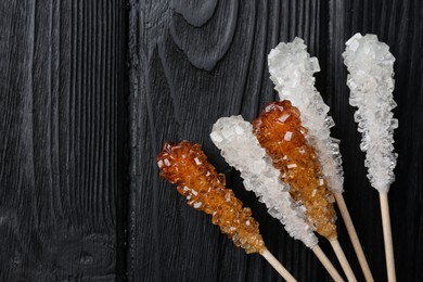 Sticks with sugar crystals on black wooden table, flat lay and space for text. Tasty rock candies