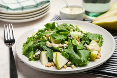 Tasty salad with pear slices, lettuce and pine nuts on table, closeup