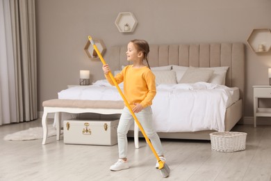 Photo of Cute little girl with broom singing while cleaning in bedroom