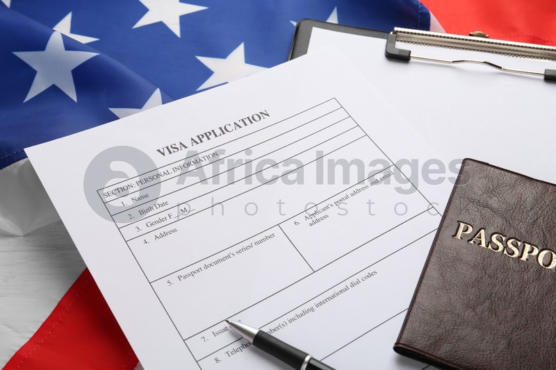 Photo of Visa application form, clipboard and passport on American flag, closeup