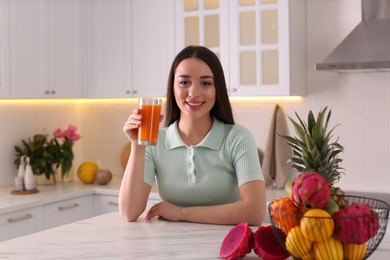 Photo of Young woman with glass of juice and exotic fruits in kitchen