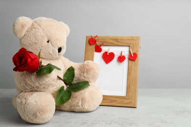 Cute teddy bear with red rose and frame on light grey stone table. Valentine's day celebration